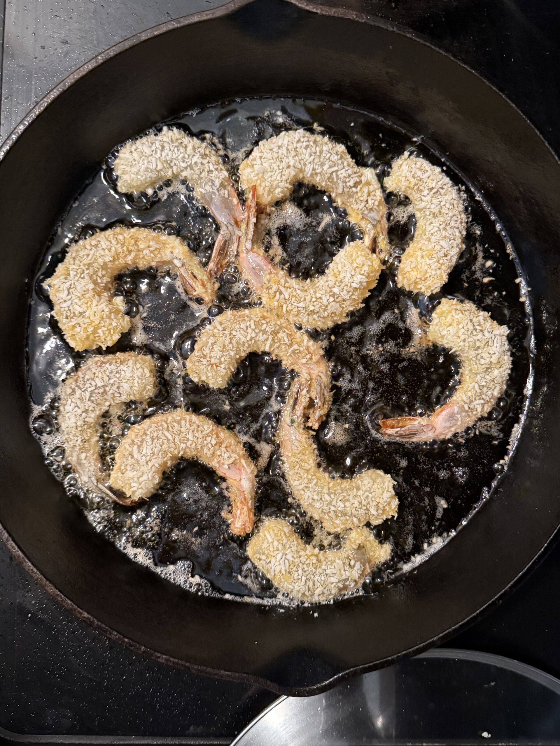 Coconut shrimp frying in avocado oil in a cast iron skillet.