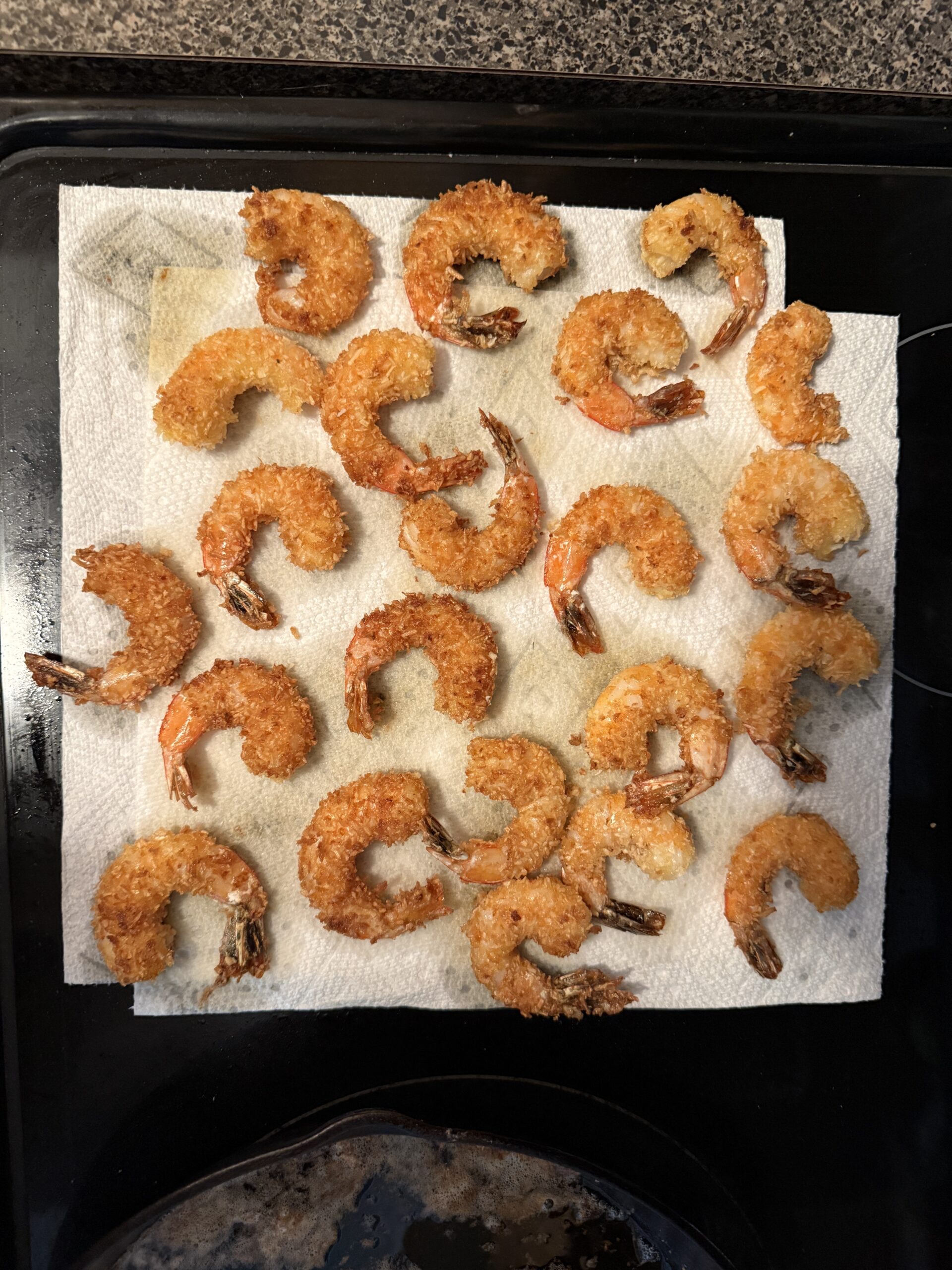Freshly fried coconut shrimp draining on a paper towel before serving.