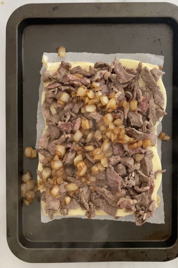 bottom of rolls, cheese, cooked steak, cooked onions layered